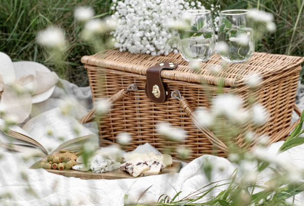 a picnic basket with flowers and cheese on a blanket